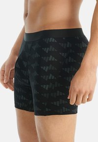 Svarta boxerkalsonger med ett geometriskt mönster i olika nyanser av mörkgrått, med ett svart elastiskt midjeband och en slät, åtsittande textur.