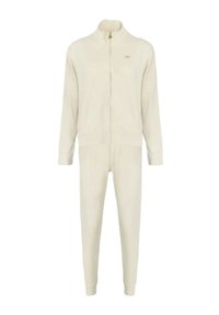 Tuta color crema composto da giacca con zip e pantaloni affusolati, realizzato in tessuto morbido con costine evidenti e un discreto logo dorato.