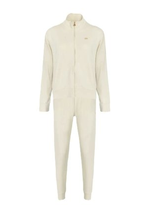 Tuta color crema composto da giacca con zip e pantaloni affusolati, realizzato in tessuto morbido con costine evidenti e un discreto logo dorato.