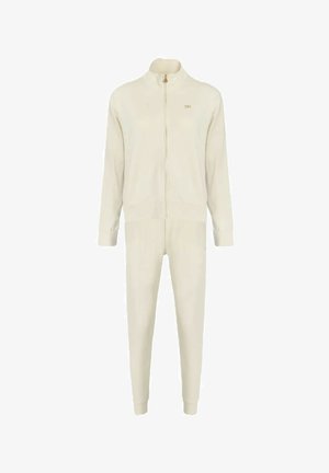 Tuta color crema composto da giacca con zip e pantaloni affusolati, realizzato in tessuto morbido con costine evidenti e un discreto logo dorato.