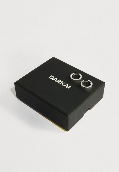 Hõbedased rõngaskõrvarõngad, millel on väikesed kivikesed, musta DARKAI kaubamärgiga karbi peal valge taustaga.