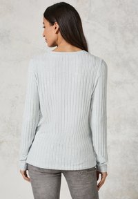 Pull en maille côtelée gris clair avec des manches longues et un col rond. Texture douce avec un ourlet droit et une silhouette cintrée.