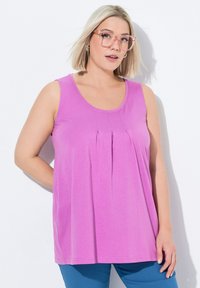 Rosa ärmelloses Oberteil mit rundem Kragen und Falten-Detailing an der Vorderseite, aus weichem Stoff, getragen mit blauen Hosen.