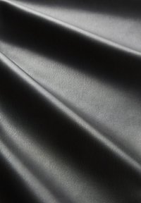 Tissu en cuir noir lisse avec des reflets lumineux subtils mettant en valeur les plis délicats et la texture fine.