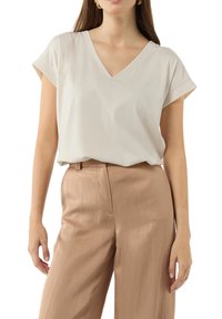 Jasno-beżowy top z dekoltem w serek i krótkimi, podwijanymi rękawami, w zestawieniu z jasnobrązowymi, luźnymi, fakturowanymi spodniami. Gładki materiał, minimalne wykończenia.