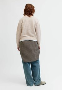 Beige stickad tröja, rutigt brunt kjol med längre baksida, avslappnade blå jeans och grå träskor. Mjuk textur, avslappnad passform.