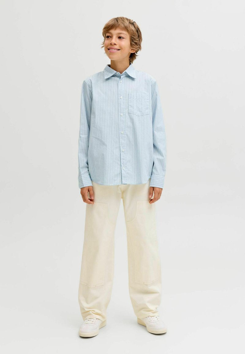 Světle modrá pruhovaná košile s knoflíky a kapsou, v kombinaci se smetanovými širokými kalhotami a bílými teniskami. Jednoduchý design a volný střih.