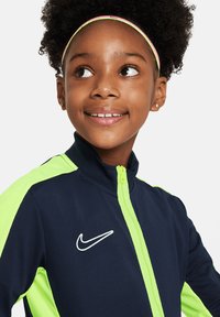 Veste Nike bleu marine et vert fluo avec un col montant, fermeture éclair intégrale et logo sur la poitrine gauche ; dispose de manches et d'épaules texturées.
