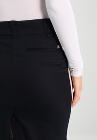 Falda azul marino con un diseño ajustado, que cuenta con bolsillos laterales y una abertura en la parte posterior. La tela parece suave, con un logo de acento dorado.