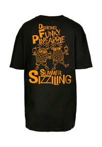 Sort t-shirt med orange grafisk tekst og to tegnefilmsagtige ananasser, der holder drinks, med teksten "Dancing Funky Pineapple Summer Sizziling."