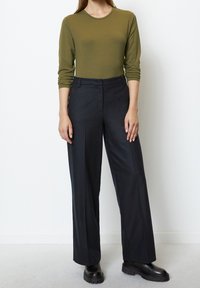 Olivgrön långärmad topp tillsammans med svarta vida byxor och kraftiga svarta stövlar, vilket skapar en strukturerad, minimalistisk outfit.