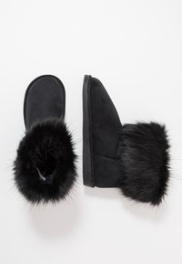 Czarne zamszowe botki z sztucznym futrem, okrągłym noskiem, niskim cholewką sięgającą kostki i czarną gumową podeszwą. Teksturowane futro dodaje szczegółów projektowi.