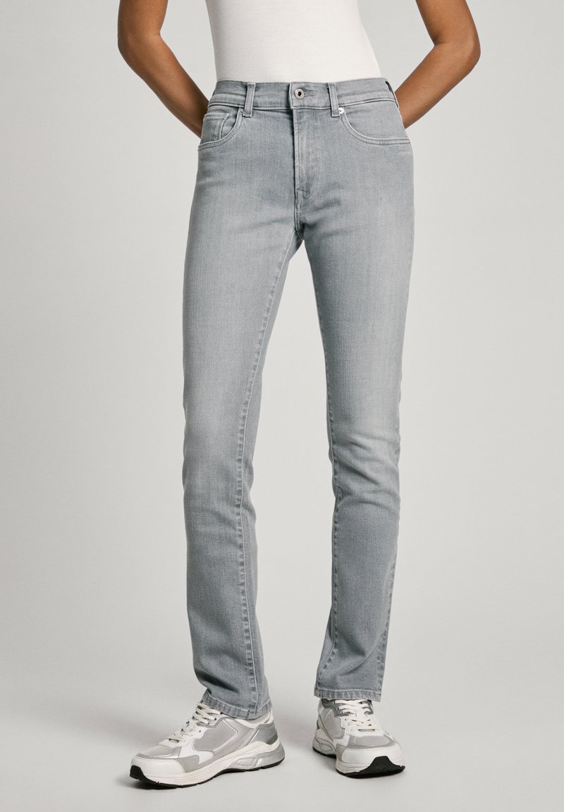 Vaqueros de mezclilla gris claro con un ajuste slim, cintura de media altura, diseño de cinco bolsillos y detalles de costura sutiles. Combinados con zapatillas atléticas grises.