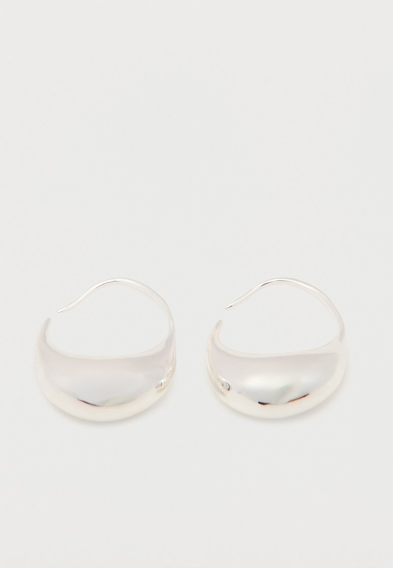 Par de pendientes de aro plateados brillantes en forma de media luna con superficies lisas y redondeadas y ganchos curvos delgados sobre un fondo blanco sencillo.