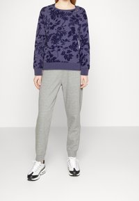 Námorně modrý sweatshirt s květinovým vzorem a knoflíky na rameni, kombinovaný se světle šedými zúženými tepláky a černobílými teniskami.