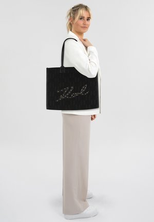 Borsa tote nera con tessuto testurizzato, caratterizzata da un motivo in rilievo scritto embellito con perle. Manici lunghi neri, forma rettangolare.