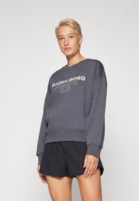 Sudadera de algodón gris con "BJÖRN BORG ATHLETIC CLUB" impreso en blanco. Corte holgado con cuello redondo y puños de canalé. Combinada con pantalones cortos negros.