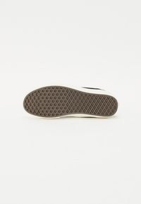 Shoe sole with a thick, textured brown rubber surface featuring a diamond pattern, and a cream-colored edge. Minimalist design, no additional details.