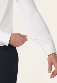 Witte lange mouwen shirt dat bij de pols wordt getrokken, met een klassieke manchet en een gladde textuur, een getailleerde pasvorm en een minimaal ontwerp.