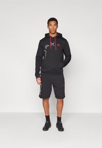 Svart hoodie med röda snoddar och logotyp, matchad med svarta shorts. Båda är tillverkade av mjukt tyg och har sidodekorationer och logotyper.