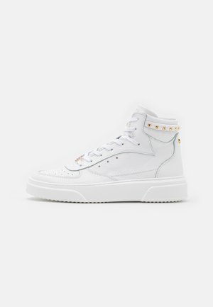 Baskets montantes en cuir blanc avec lacets à l'avant, accents de clous dorés sur la bride cheville et semelle texturée sur fond uni.