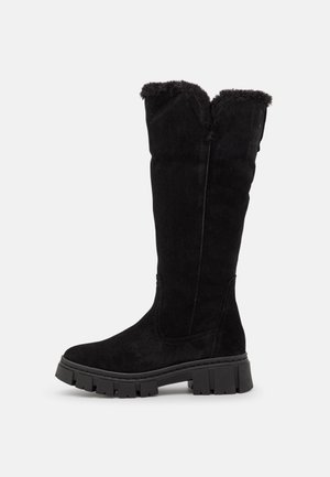 Korkea musta mokkanahkainen talvinaurus, jossa on turkisreunus ja paksu kulutuspohja, esitetty sivulta valkoisella yksinkertaisella taustalla.