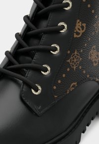 Bottines noires à lacets avec une finition en cuir lisse et un panneau texturé marron à motifs comprenant des logos. Œillets en argent et lacets noirs.