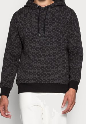 Hoodie noir avec un motif répétitif de logo "CK" gris clair, capuche avec cordon de serrage et poignets et ourlet côtelés. Tissu doux.