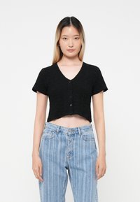 Haut noir à manches courtes et coupe courte en tissu texturé, avec un devant à boutons, associé à un jean bleu rayé taille haute.