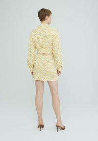 Geel gemusterde crop top en bijpassende rok, met een golvend ontwerp, lange mouwen en een aansluitende silhouet, gecombineerd met bruine hoge hakken.