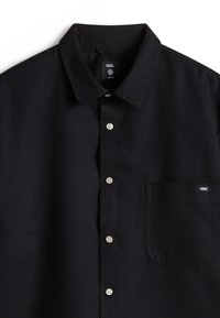 Camisa negra de botones fabricada en algodón, con cuello, un bolsillo en el pecho izquierdo y botones blancos en contraste. Textura sutil visible.