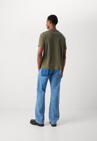 Oliven grøn kortærmet t-shirt kombineret med lyseblå denim jeans. Jeansene har et patch-lomme detaljer og en afslappet pasform. Sorte sko.