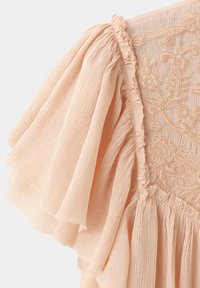 Manche de robe rose clair avec tissu plissé, bords à volants et broderie florale sur le corsage.