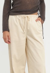 Beige corduroy broek met een brede pijp, voorzien van zijzakken en een trekkoord in de taille. De stof heeft een subtiele ribbelstructuur.