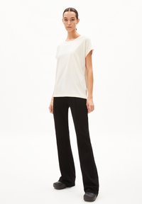 T-shirt à manches courtes couleur crème associé à un pantalon noir évasé. Le T-shirt a un design simple ; le pantalon a une texture lisse et une silhouette élégante.