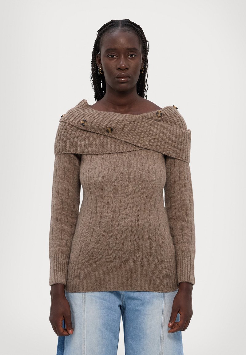 Brauner Strickpullover mit weitem, umgeschlagenem Kragen und Knopfverzierungen, gerippter Textur und taillierten Ärmeln. Kombiniert mit hellblauen Jeans.