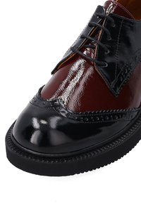 Hnědé a černé kožené společenské boty s lesklým povrchem, designem wingtip, brogue detaily a černou gumovou podrážkou. Jsou přítomny tkaničky.