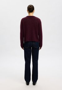 Vinröd kort tröja med en slät textur, kombinerad med mörkblå raka jeans. Outfiten har en minimalistisk design och rena linjer.