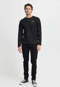 Fekete hosszú ujjú póló, kerek nyakkivágással és hímzett logóval, fekete slim-fit farmernadrággal és fekete sportcipővel párosítva.