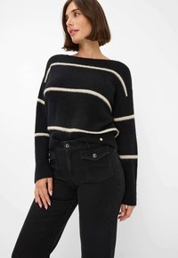 Maglione a righe nere con linee orizzontali beige, caratterizzato da una vestibilità ampia e polsini a costine, abbinato a jeans neri a vita alta.