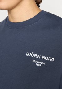 Námorníckomodrá bavlnená tričko s okrúhlym výstrihom, na prednej strane s bielym vyšívaným textom "BJÖRN BORG" a "STOCKHOLM 1956".