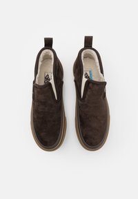 Chaussures à enfiler en daim marron avec une doublure douce, dotées d'un côté élastique beige et d'une semelle en caoutchouc avec un accent brun clair.