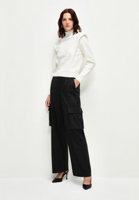 Witte trui met een hoge kraag en reliëfontwerp, gecombineerd met zwarte cargo broek met een streepje, voorzien van zijzakken en wijde benen.