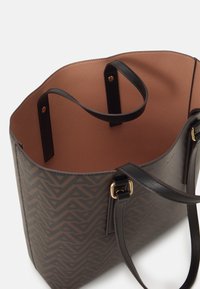 Torba tote w ciemnym wzorze z geometrycznym wzorem. Posiada gładkie czarne uchwyty oraz beżowe strukturalne wnętrze. Występują złote akcenty metalowe.