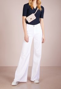Top de punto en tono marino con escote en V, pantalones de pierna ancha de talle alto en blanco, bolso crossbody beige con logo y zapatillas blancas con rayas negras.