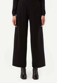 Svarta vida byxor i mjukt stickat material, med ett elastiskt midjeband och slät yta, i kombination med svarta ankelstövlar.