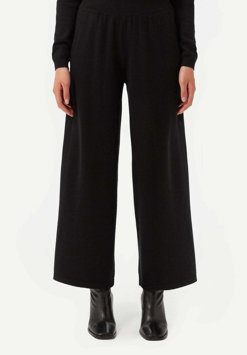 Svarta vida byxor i mjukt stickat material, med ett elastiskt midjeband och slät yta, i kombination med svarta ankelstövlar.