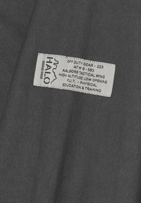 Grauener Stoff mit einem strukturierten, gerippten Design. Ein weißes Etikett mit schwarzem Text enthält Details zum Produkt und zum Hersteller.