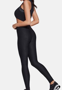 Czarny komplet sportowy składający się z teksturowanego krótkiego topu i legginsów z wysokim stanem o wzorze plastra miodu, uzupełniony eleganckimi czarnymi sneakersami.