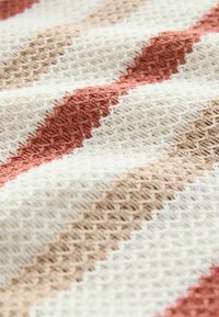 Tekstilstof med et vævet mønster bestående af skiftende striber i creme, beige og terracotta farver. Tekstureret overflade med en blød fornemmelse.